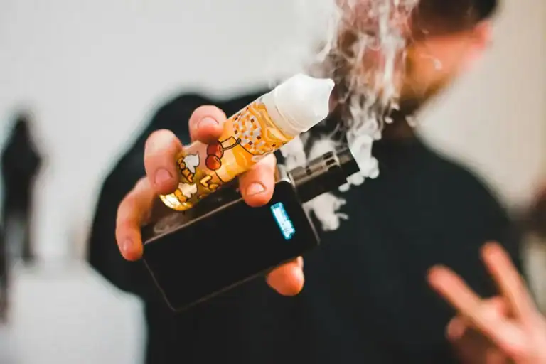 手持電子煙主機與煙油瓶,背景可見電子煙蒸氣